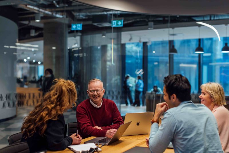 Four people seated at a table, each working on a computer