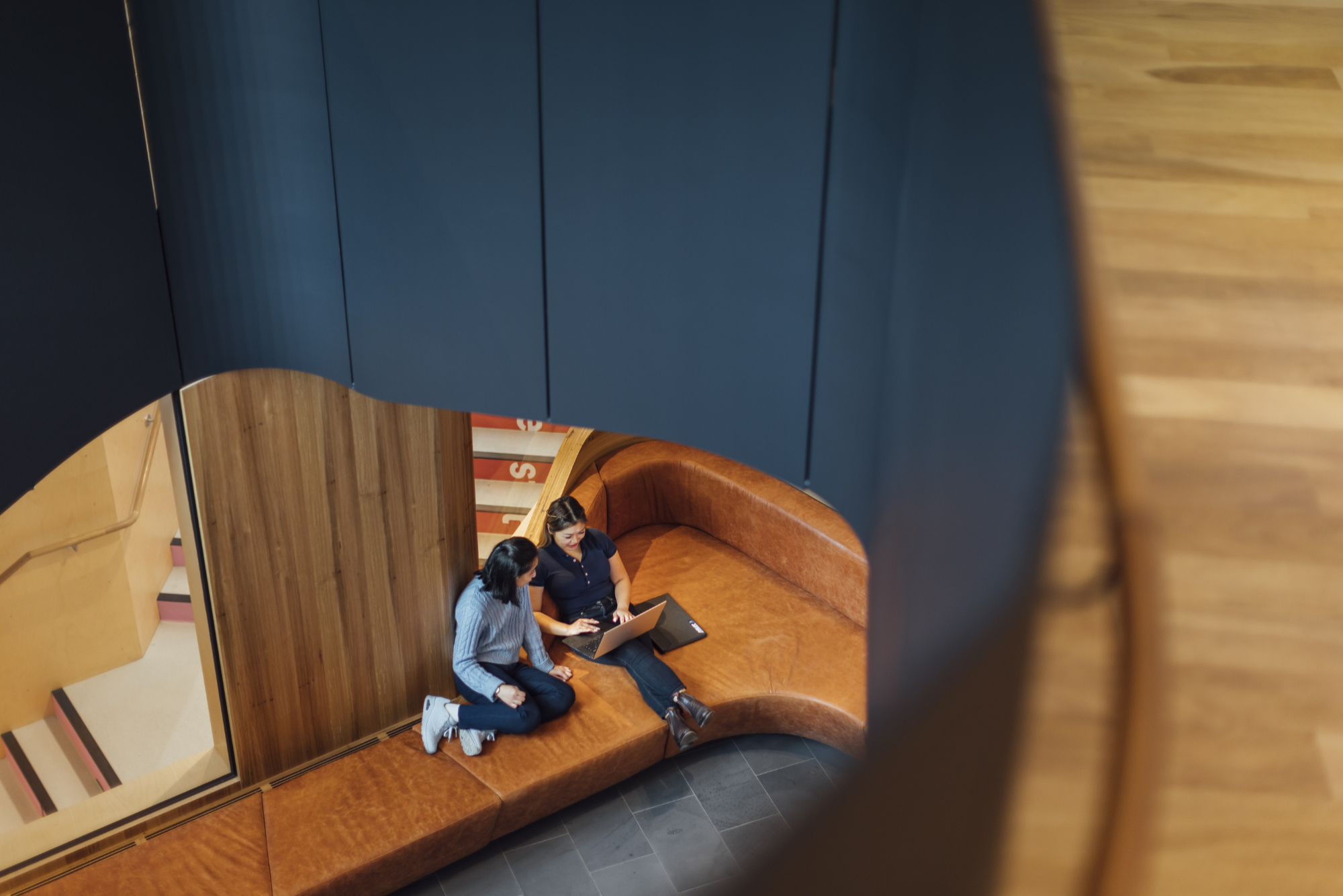 Two students sitting on leather couches with laptops studying